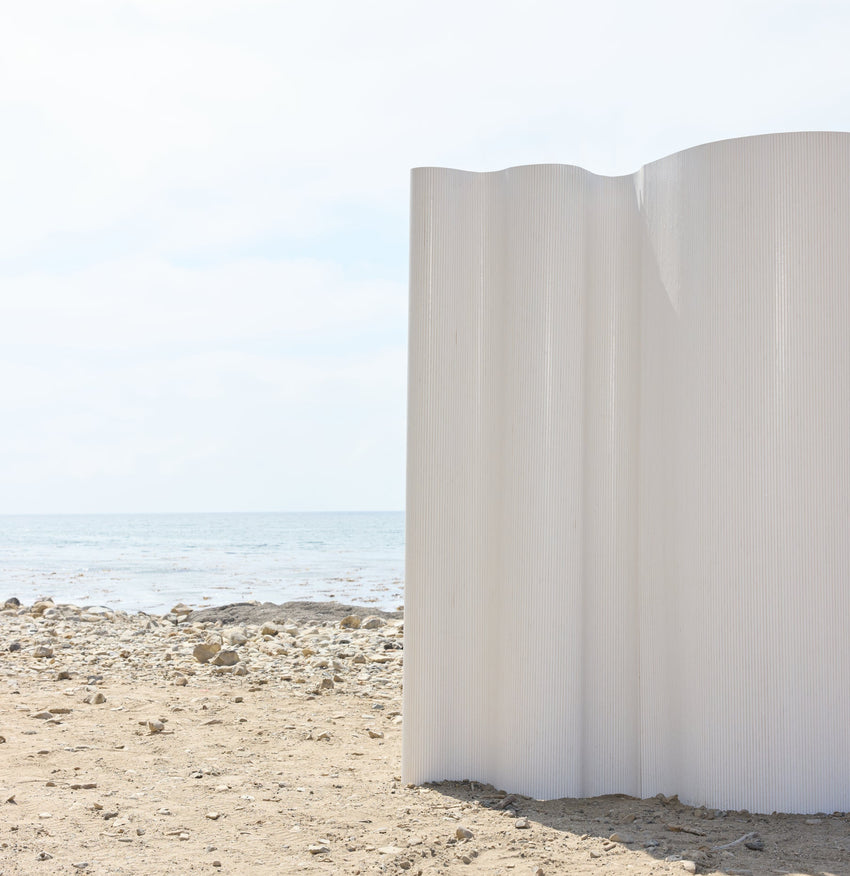 White sculptural installation on a sandy beach with ocean and sky in the background.