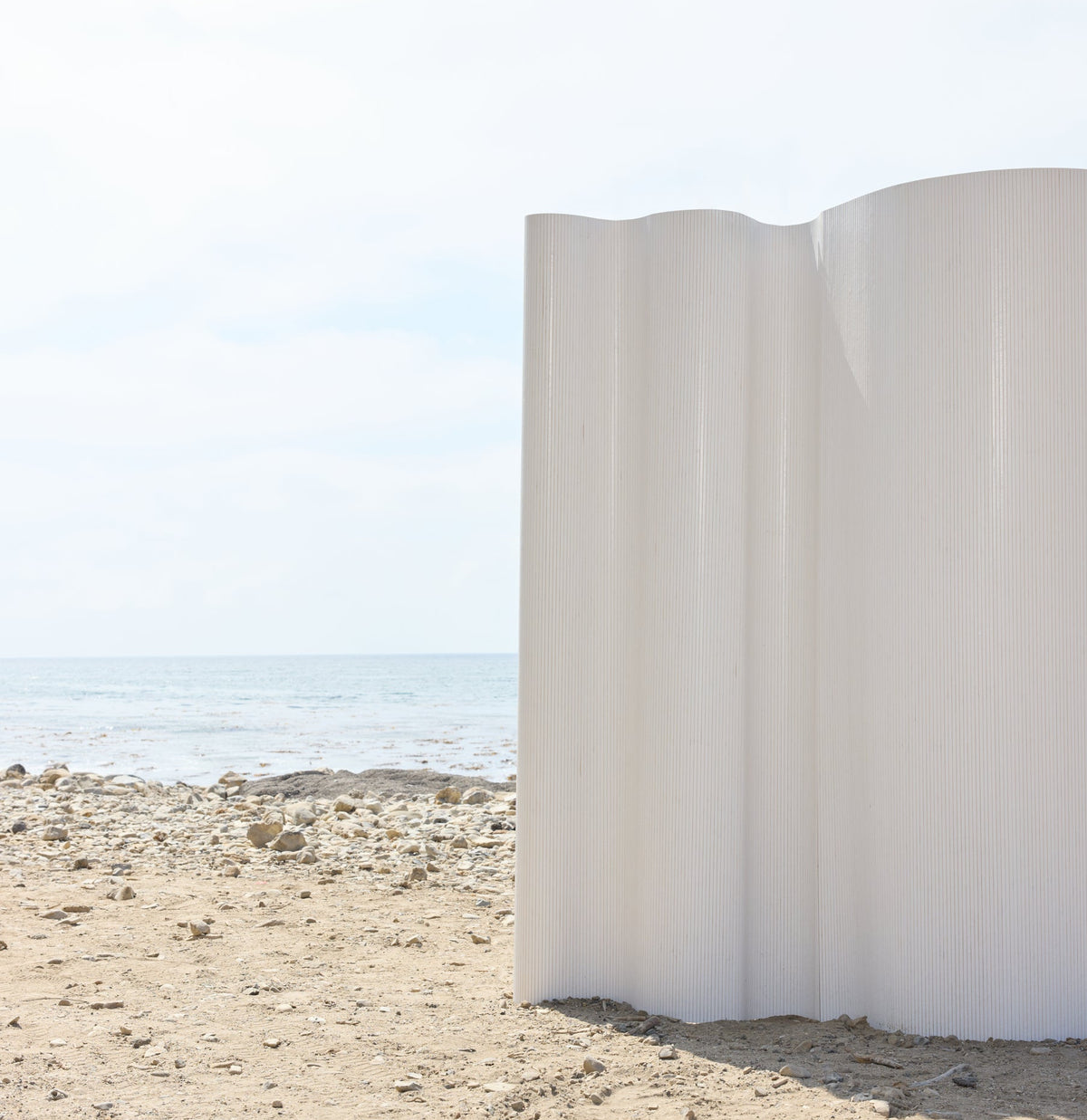 White sculptural installation on a sandy beach with ocean and sky in the background.