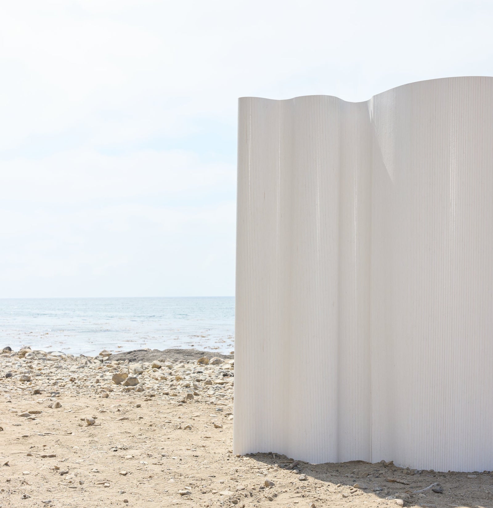 White sculptural installation on a sandy beach with ocean and sky in the background.